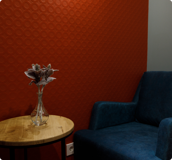 Фото стола с искусственными цветами в вазе, на заднем фоне синее кресло